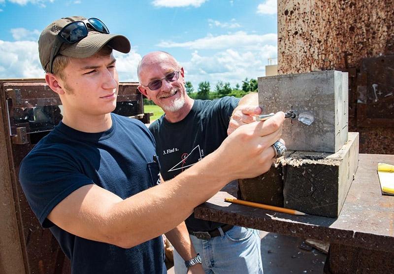 A cadet and a researcher work with a block of aluminum.